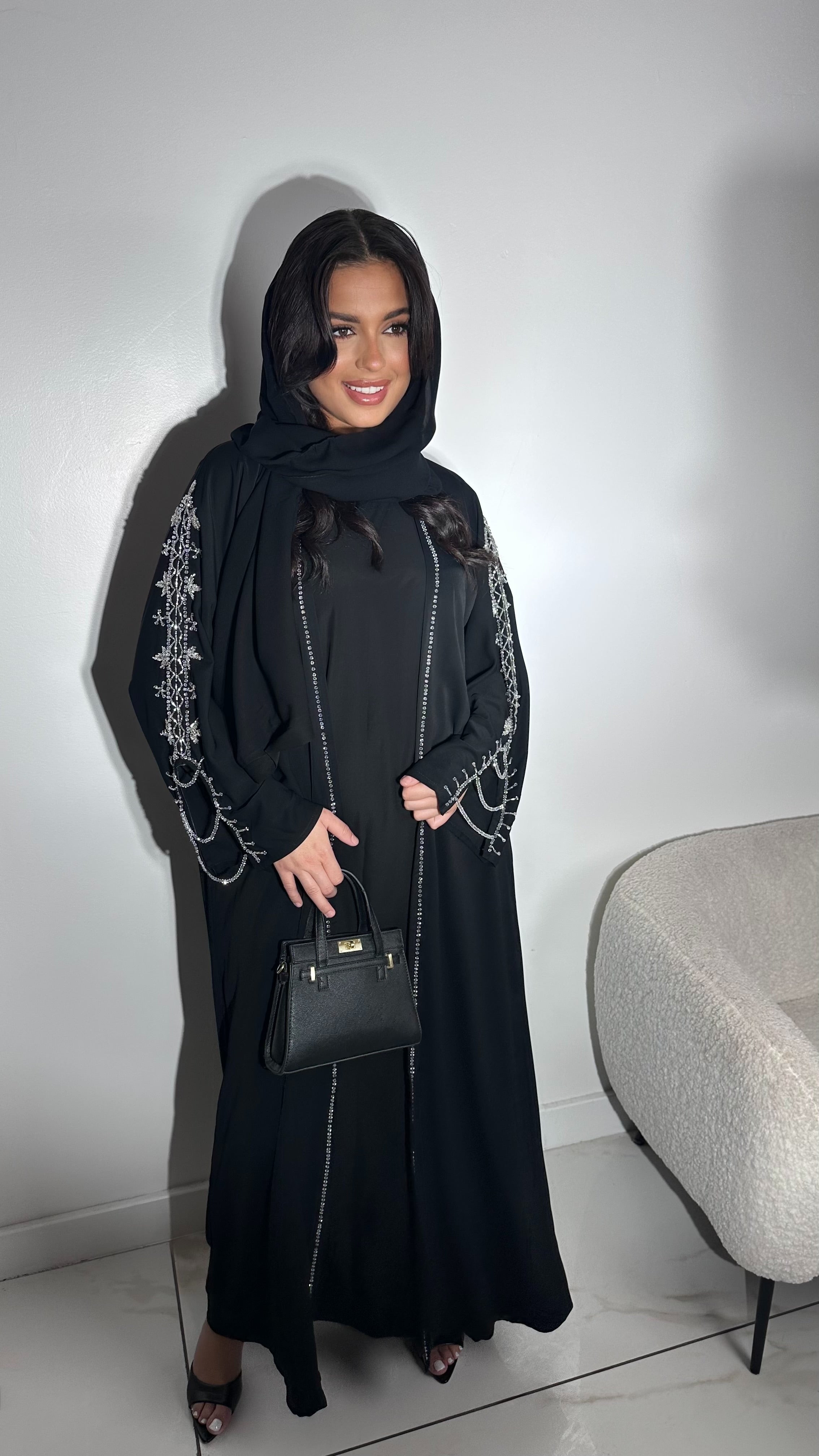 Tissu Nidha fluide Ouverture sur l'avant-bras, rehaussée de strass reliant les deux pans de la manche Perlage cousu à la main sur les bras Sous robe assortie incluse Ceinture ton sur ton Voile intégré Confectionnée à Dubaï